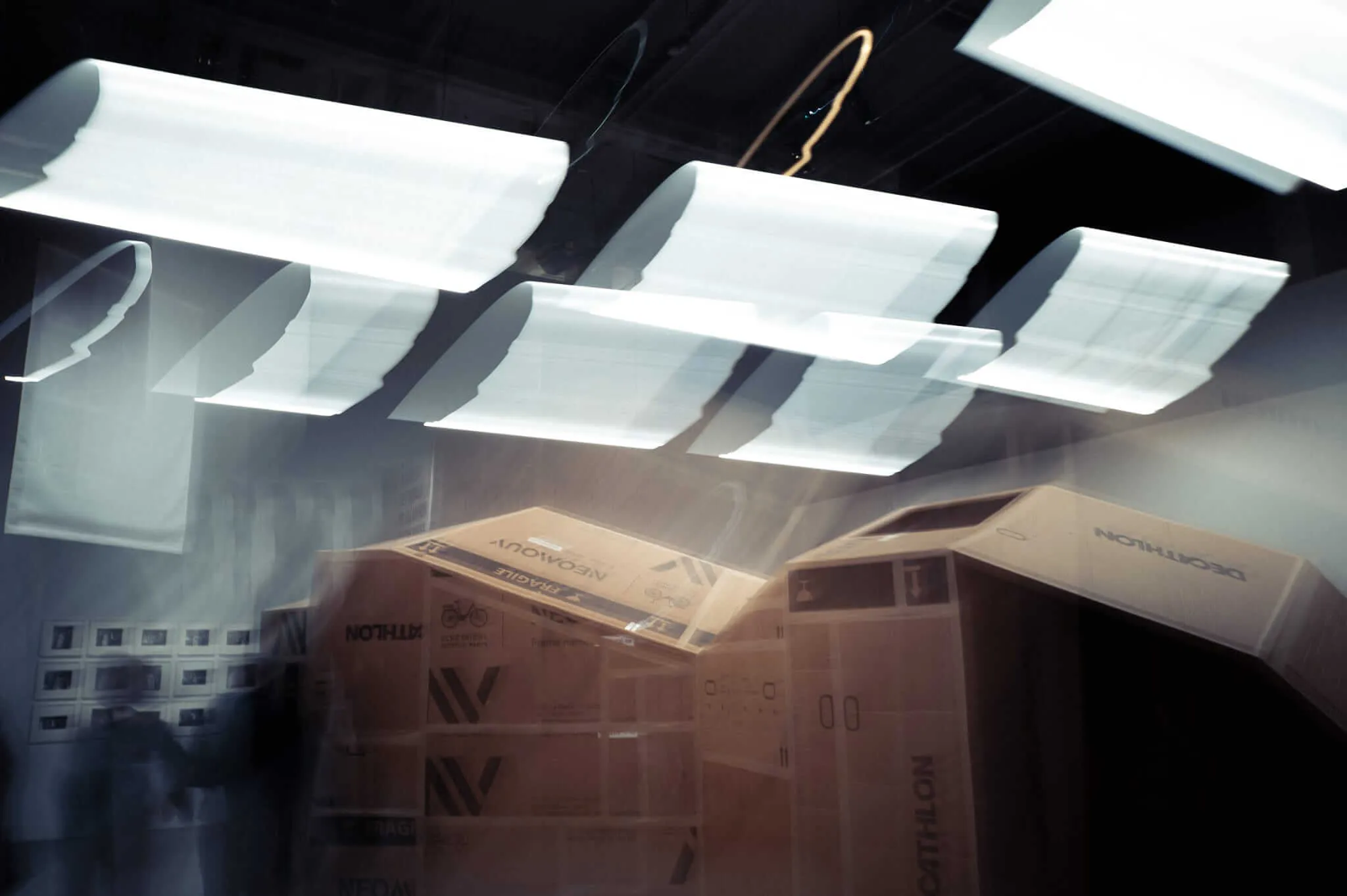 Interior view of a car trunk filled with stacked cardboard boxes, photographed from inside looking up through the rear window at bright white panels of sky or ceiling, creating geometric patterns of light and shadow